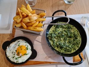 a fried egg and a skillet of creamed spinach in front of a basket of french fries