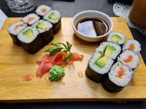Salmon and avocado rolls on a wooden chopping board with fresh ginger, wasabi ,and soy sauce