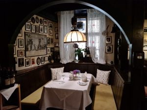 Restaurant interior. An arched nook with a wall of photos on the left, a white ceramic lamp over a table dessed in a white tablecloth