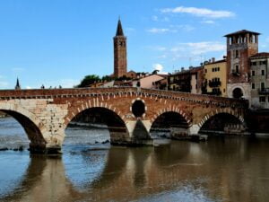 arched stone bridge (Ponte Pietra) spanning the Adige River in Verona set agains a blue sky with a church twoer in the centre background