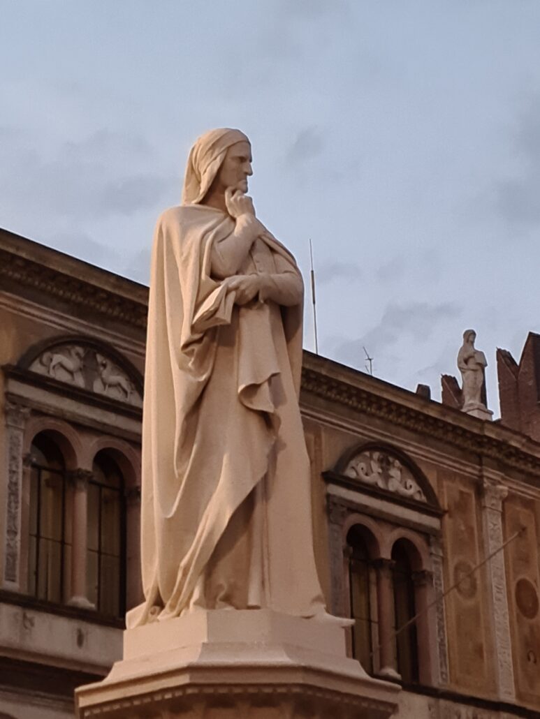 Statue of a cloaked, hooded man with a with left elbow resting on right wrist and finger under his chin in a thoughful pose