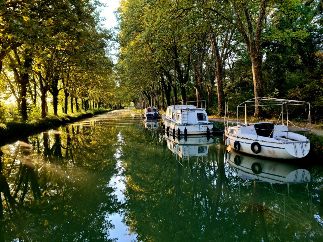 Sun coming through the trees on the canal de Garonne - three boats moored on the right hand side