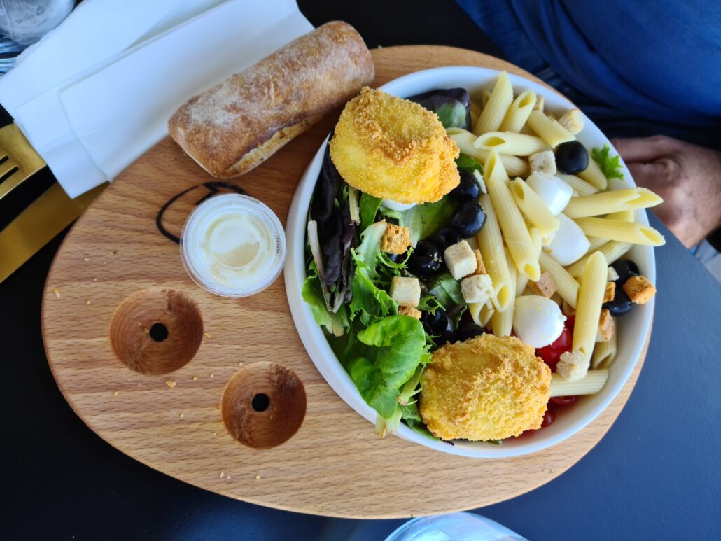 a wooder serving platter with a plate containing two crispy poached eggs with pasta and a salad
