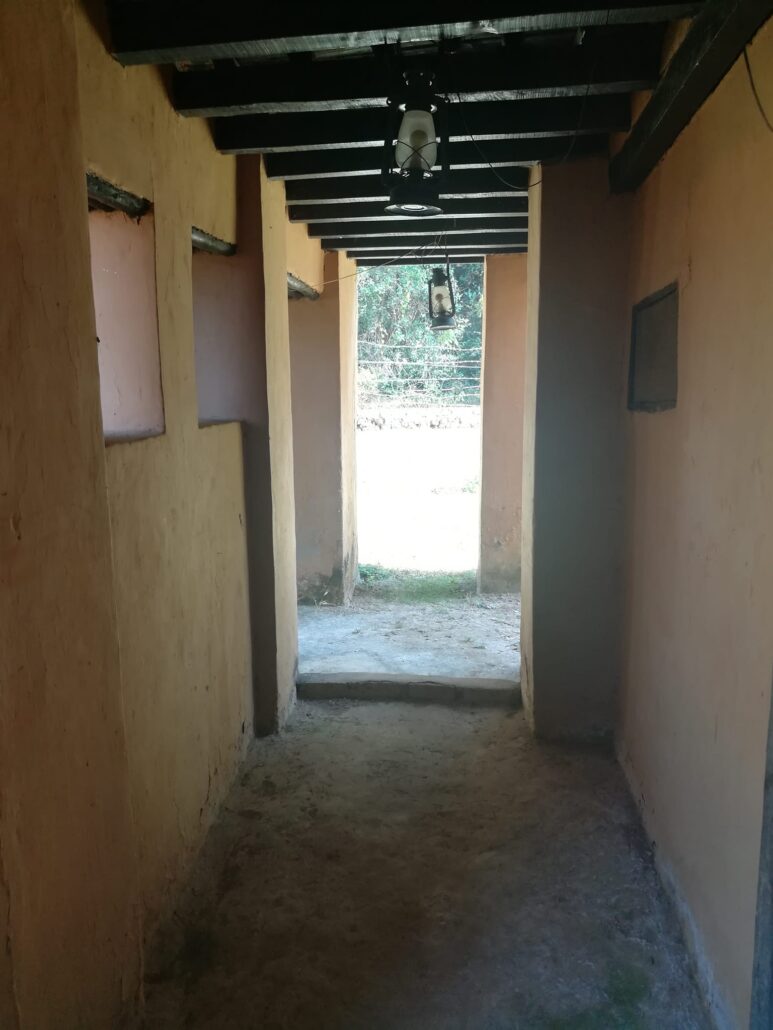 Corridor in an Indian mudwalled house with wooden beams and high windows. A lantern hangs from the ceiling