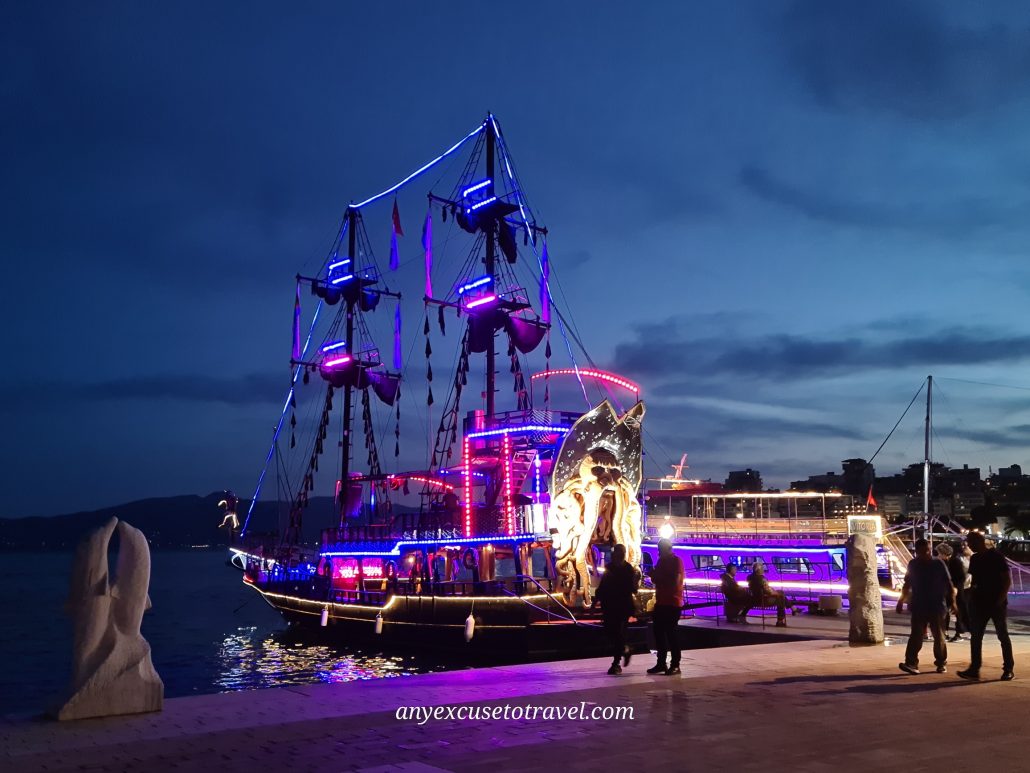 Party pirate ship lit up in pinks and purples as people mill around it taking photos