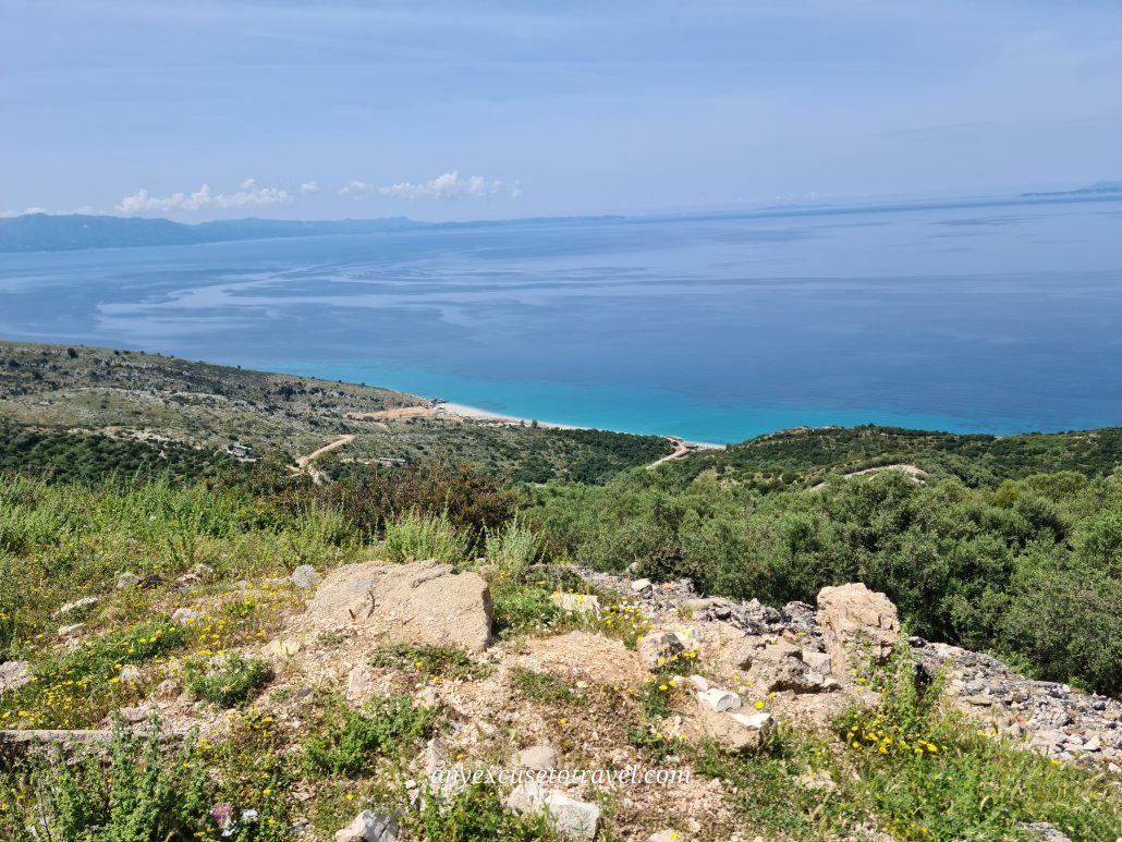 View of the water in deep turquoise close to a sandy beach. A rocky hill slopes down to the sea