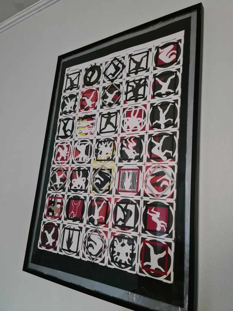 Framed picture (Black frame) of 35 squares with paper cut outs of bodies doing things for example, curled in a ball or standing on its head or climbing a wall. 