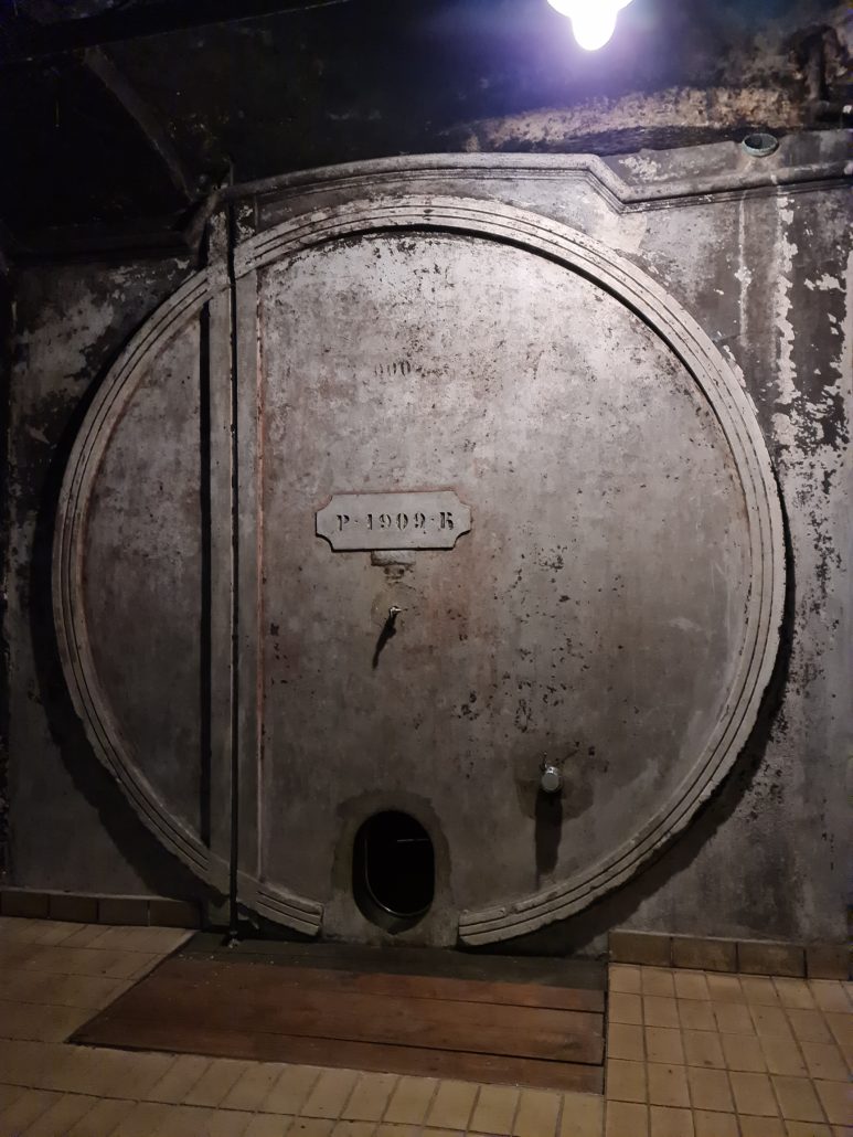 Aged, round steel door to a concete wine cellar with a plaque on front reading P 1909 R