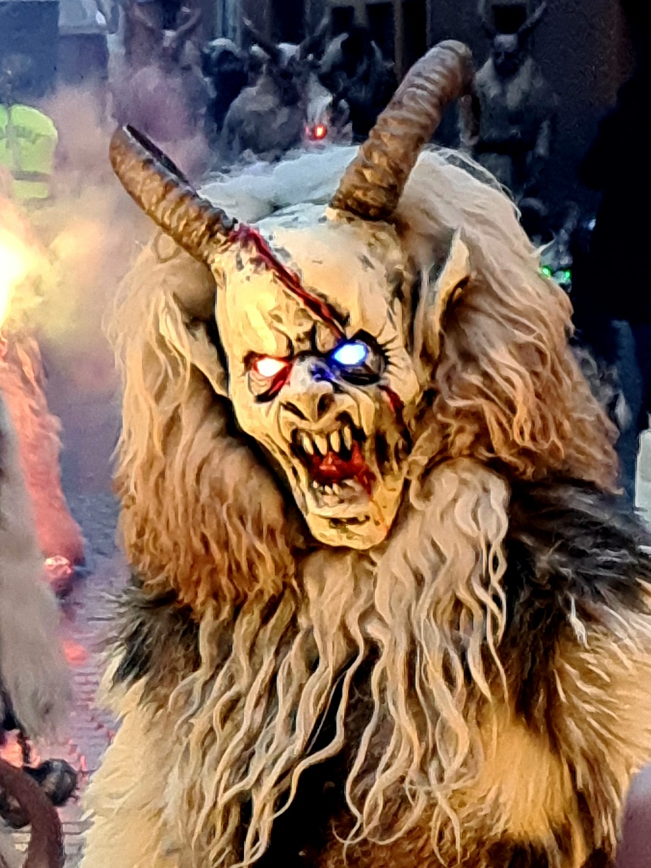 Person wearing a kurent costume - horns, devil mask with glowing eyes, wool hair - like a sheep's fleece. Gruesome teeth barred - smoke in the background