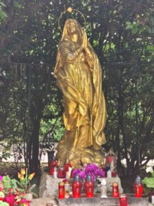 Gilded statue of the Madonna with flowers and candles at the base