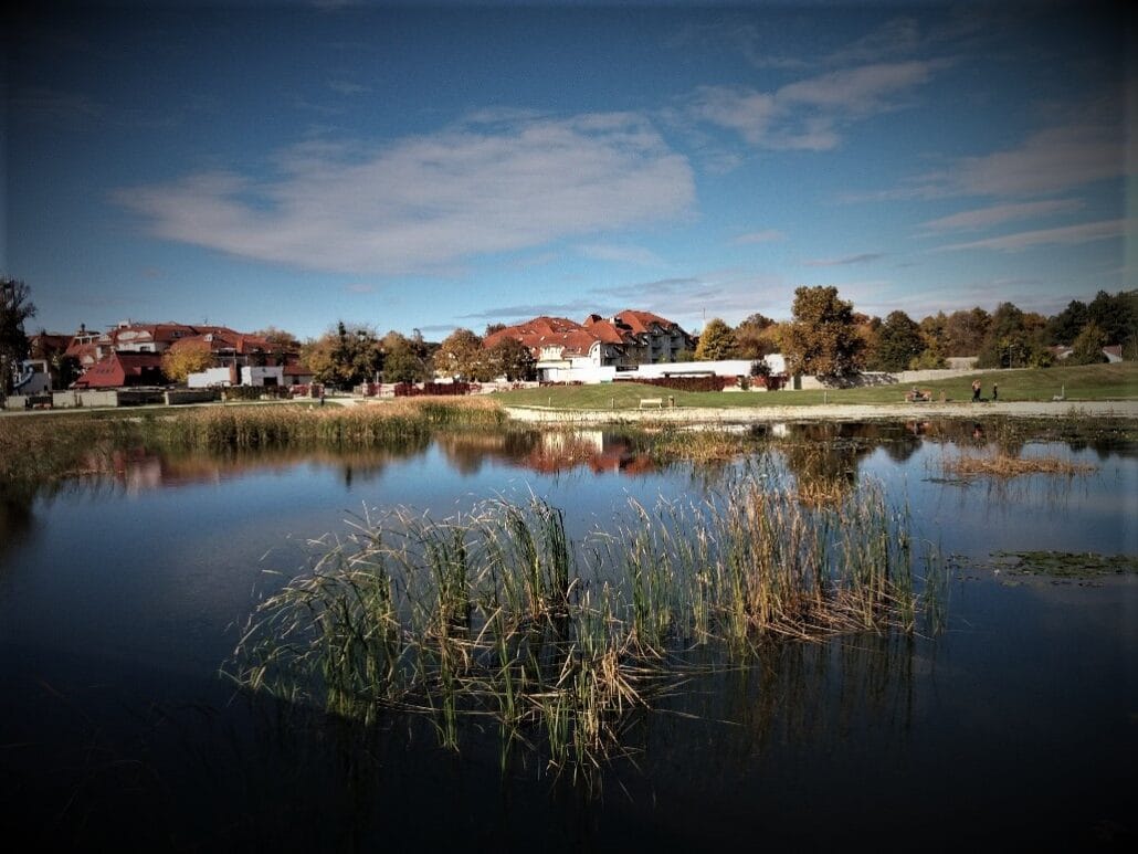 Vignette of red roofed buildings across a small lake with reed islands