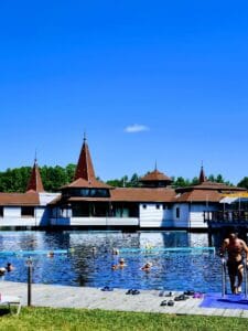 People bathing in an outdoor thermal lake with red roofed buildings in the background