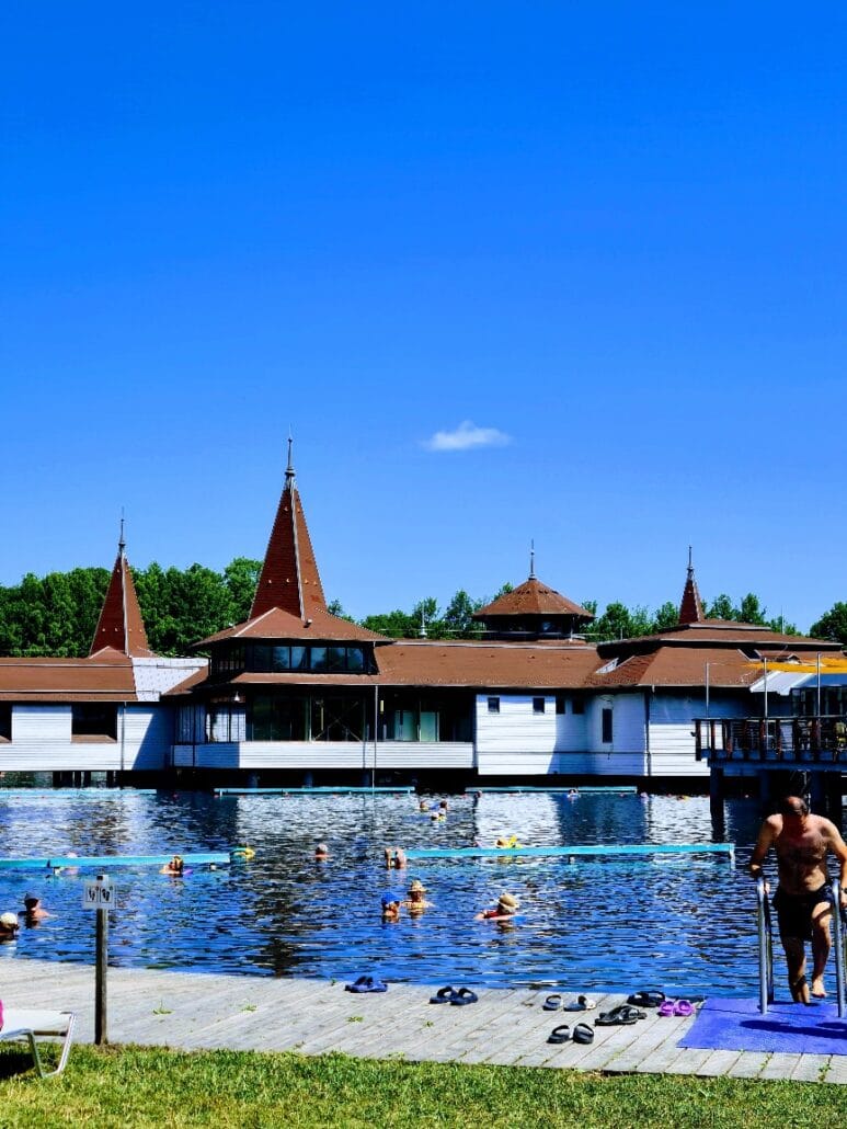 People bathing in an outdoor thermal lake with red roofed buildings in the background