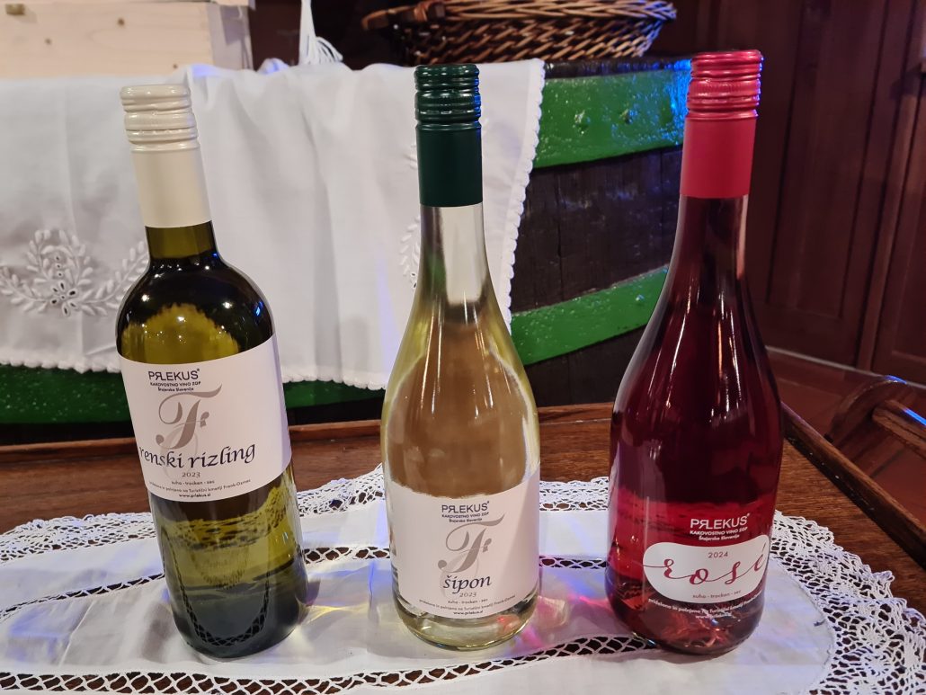 Three bottles of wine - one a Prlekus Renski rizling, the second a Prlekus sipon, and the third with a pink top - a prlekus rosé - on a lace cloth on a wooden tray 