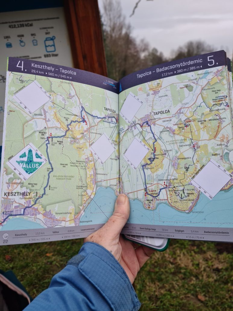 A hand holding a book of maps with the thumb keeping the pages apart - one of the six diamonds has a green stamp