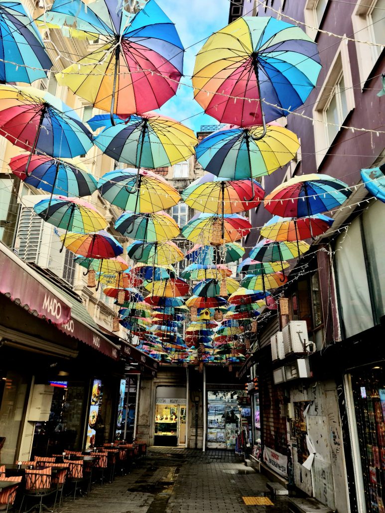 Narrow shopping street with brighly coloured umbrellas reaching from one side to the other creating a ceiling of sorts