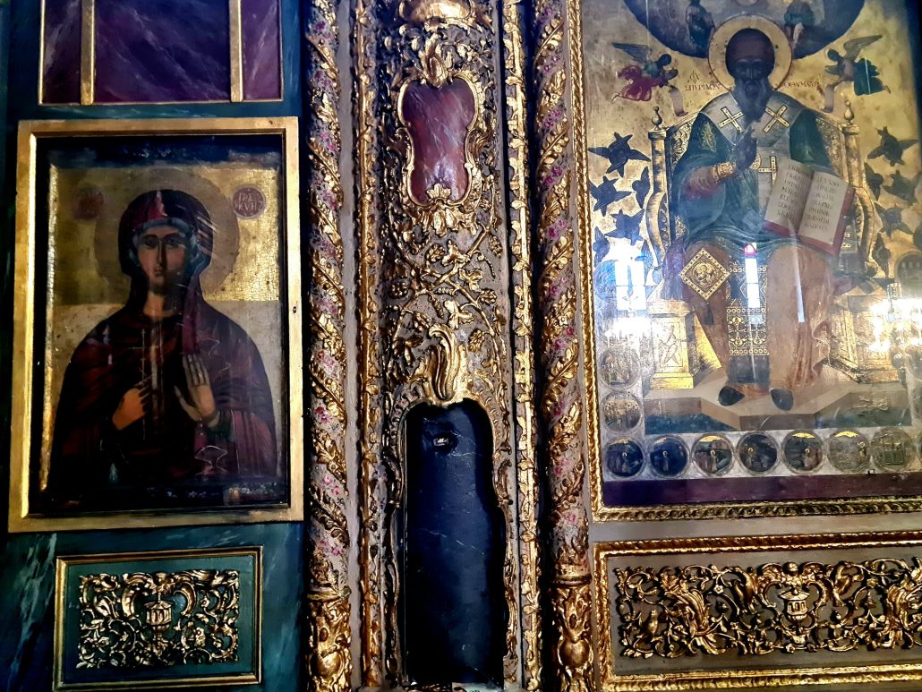 Inside an orthodox church - lots of gold and filigree work - two pieces are exposed - one longer vertical piece is a very dark brown, almost black. The upper piece is smaller and more red. Holy pictures sit either side.