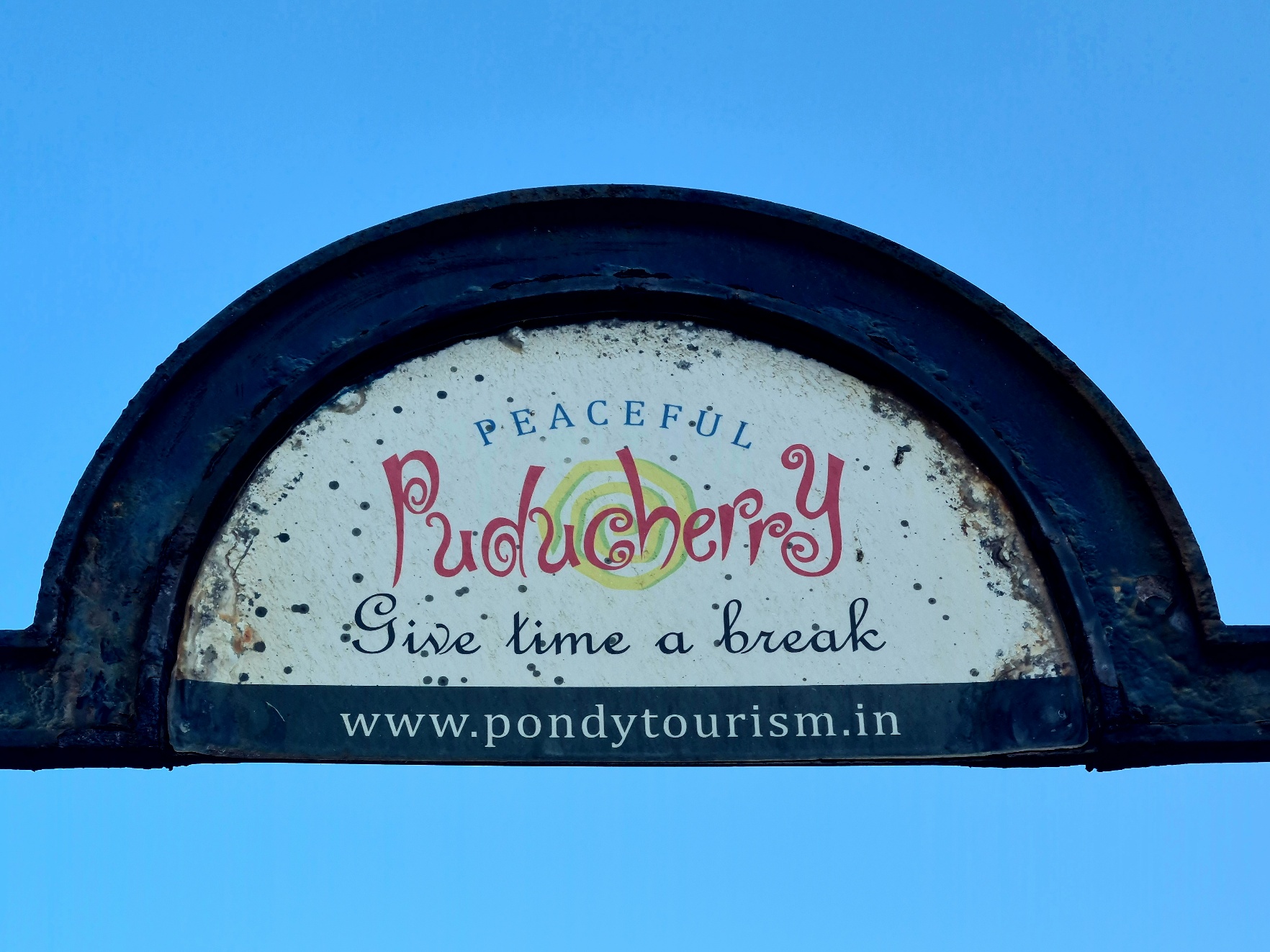 Semi-circular sign that reads Peaceful Puducherry - Give time a break