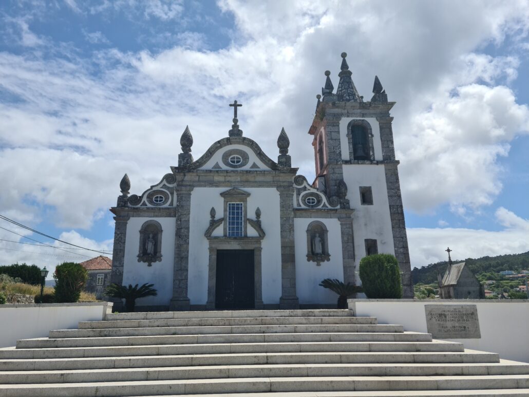 Steps leading up to a stone granite church painted white offset against a blue sky with white clouds