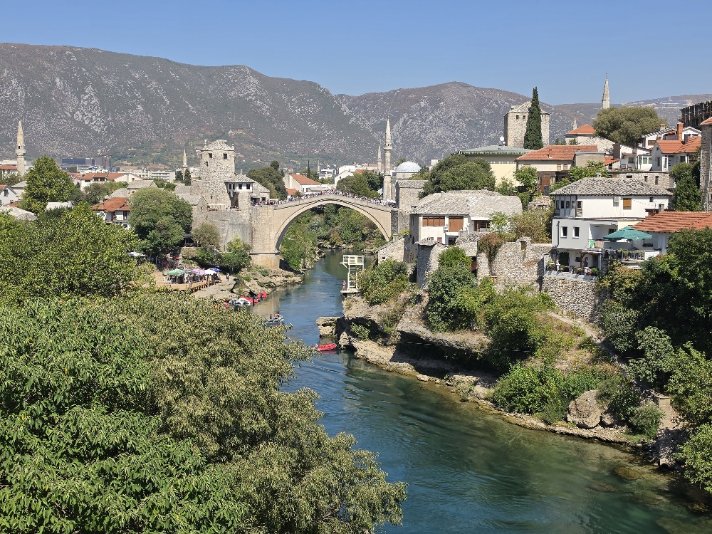 Panoramic view of Mostar, Bosnia and Herzegovina, with the historic Old Bridge spanning the Neretva River and mountains in the background.