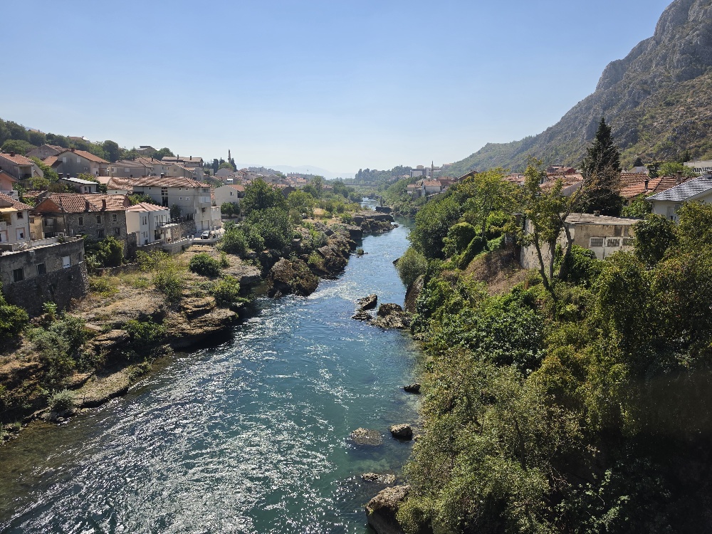 The turquoise Neretva River flowing through Mostar, with houses and steep rocky mountains along both banks.