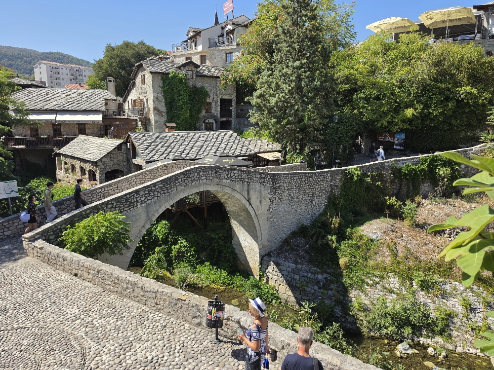 The historic stone Crooked Bridge over the Radobolja stream in Mostar's Old Town, surrounded by traditional stone buildings and restaurants.