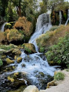 “Close view of a cascading section of Kravica Falls, with clear water flowing over moss-covered tufa rocks and dense green vegetation.”
